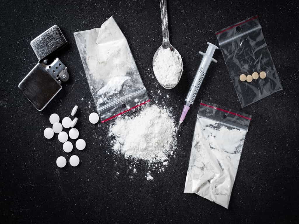 Black Table with White Power in a Bag, Pills in a Bag, a Spoon with White Powder, Syringe, & Lighter
